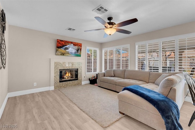 living room featuring light wood-style flooring, a ceiling fan, visible vents, and baseboards