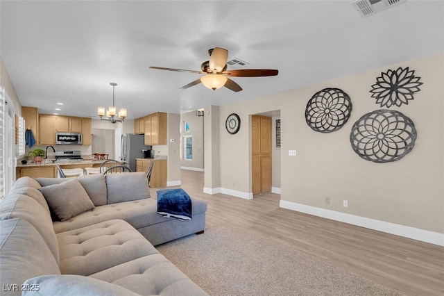 living room with visible vents, baseboards, ceiling fan with notable chandelier, and light wood finished floors