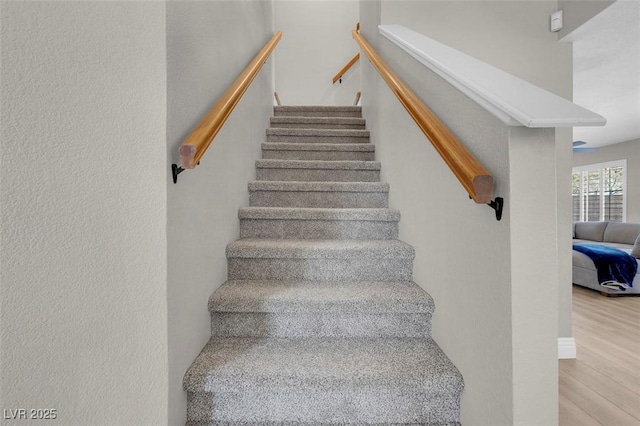 stairway featuring wood finished floors and a textured wall