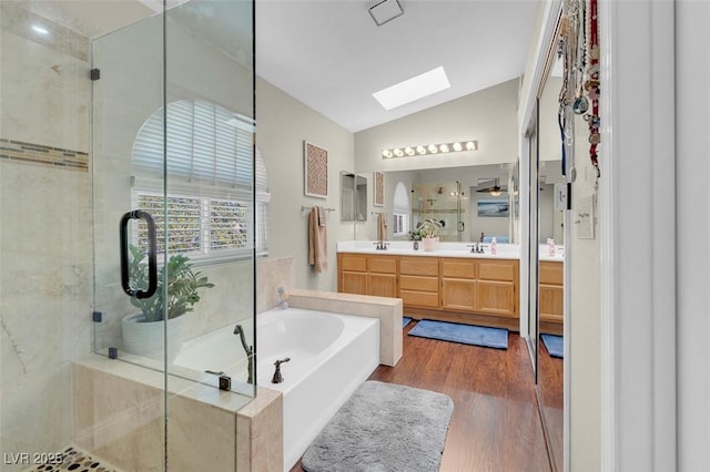 bathroom featuring a garden tub, a stall shower, wood finished floors, vaulted ceiling with skylight, and double vanity