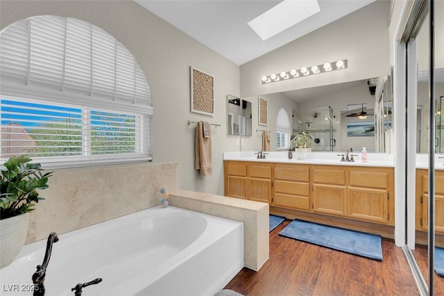 full bath featuring wood finished floors, double vanity, vaulted ceiling with skylight, a stall shower, and a garden tub