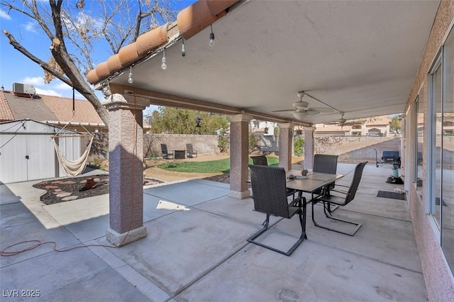 view of patio / terrace featuring a storage shed, a fenced backyard, an outdoor structure, outdoor dining area, and a ceiling fan