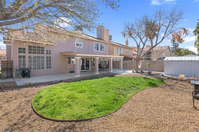 back of property with fence, a shed, stucco siding, an outbuilding, and a patio