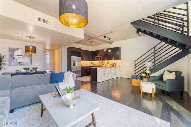 living room featuring visible vents, dark wood-type flooring, and stairway