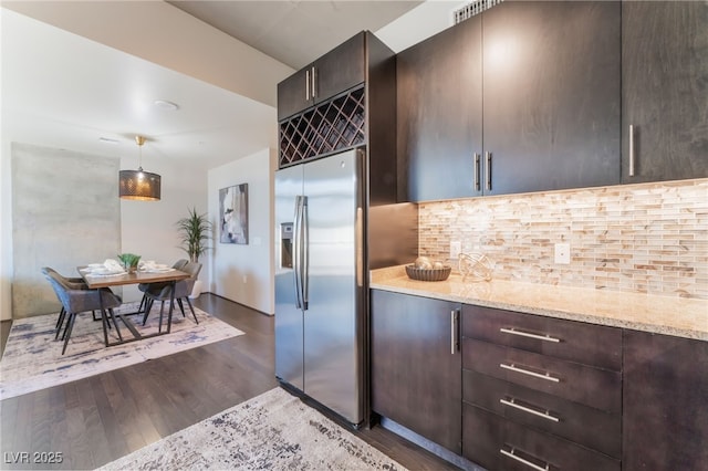 kitchen featuring light stone counters, decorative backsplash, dark wood-type flooring, and stainless steel refrigerator with ice dispenser