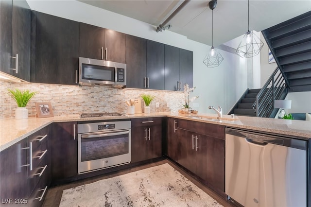 kitchen featuring backsplash, light stone countertops, hanging light fixtures, stainless steel appliances, and a sink