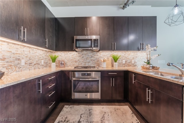 kitchen featuring pendant lighting, a sink, stainless steel appliances, decorative backsplash, and light stone countertops