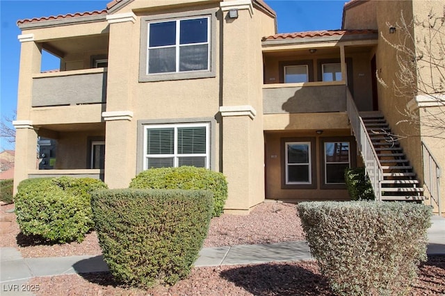 exterior space with stucco siding, a tile roof, stairs, and a balcony