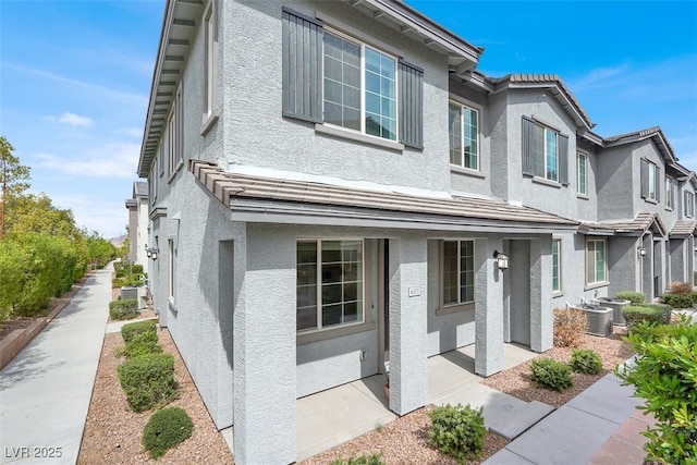 traditional home featuring stucco siding, cooling unit, and a porch