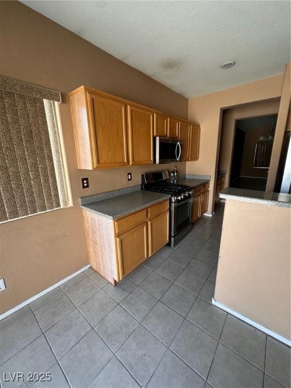 kitchen with light tile patterned floors, baseboards, a textured ceiling, and appliances with stainless steel finishes