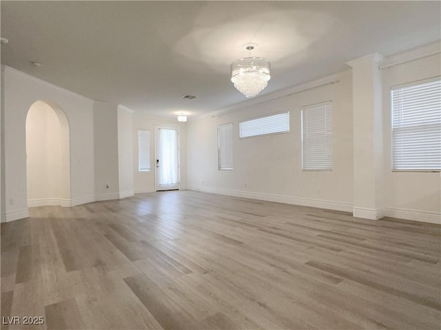 empty room featuring a chandelier, light wood-type flooring, and crown molding