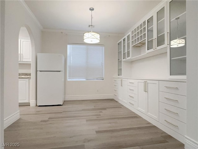 unfurnished dining area featuring baseboards, light wood-style floors, ornamental molding, and arched walkways