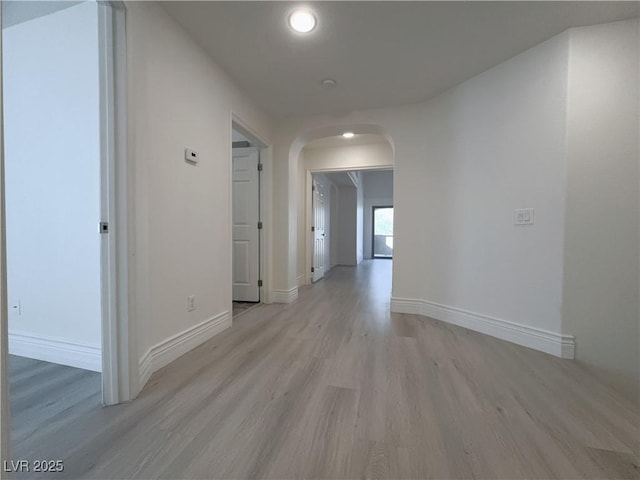 corridor with arched walkways, baseboards, and light wood-style floors