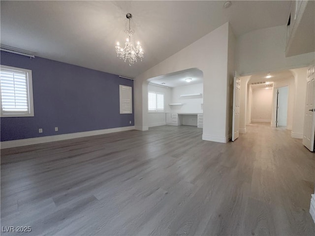 unfurnished living room with vaulted ceiling, a notable chandelier, wood finished floors, and arched walkways