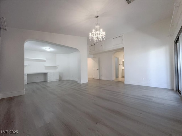 unfurnished living room featuring arched walkways, baseboards, an inviting chandelier, and wood finished floors