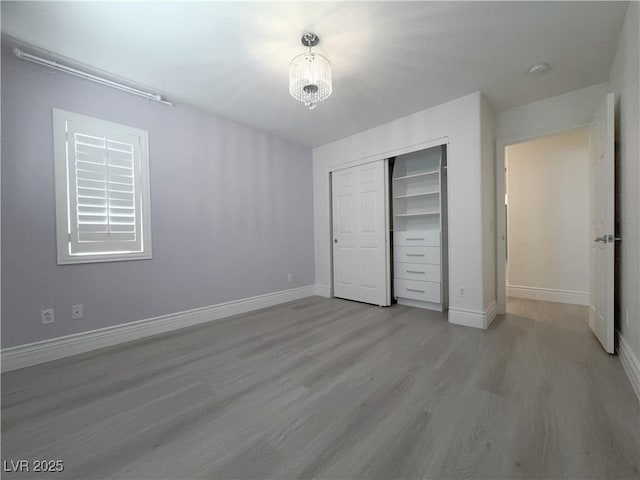 unfurnished bedroom with a notable chandelier, wood finished floors, a closet, and baseboards