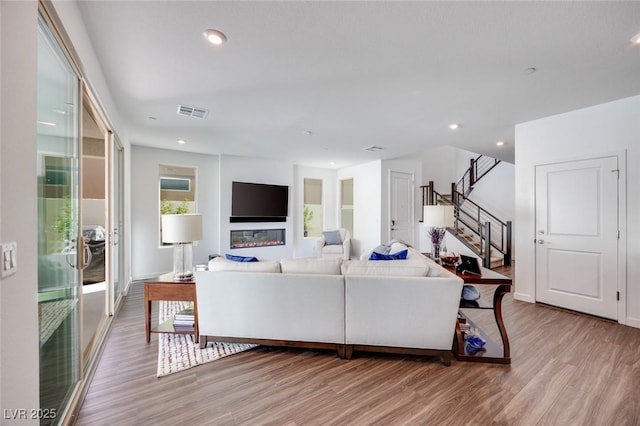 living room with wood finished floors, recessed lighting, visible vents, and stairs