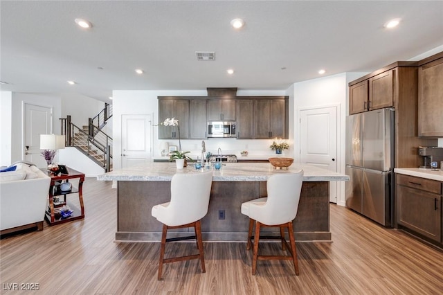 kitchen featuring stainless steel appliances, visible vents, a kitchen bar, and wood finished floors