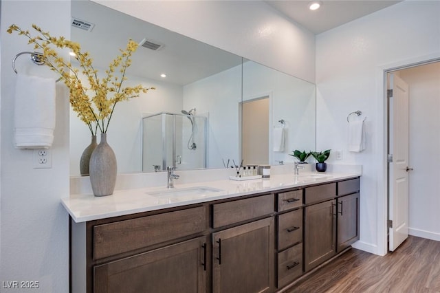 full bath with a shower stall, visible vents, wood finished floors, a sink, and double vanity
