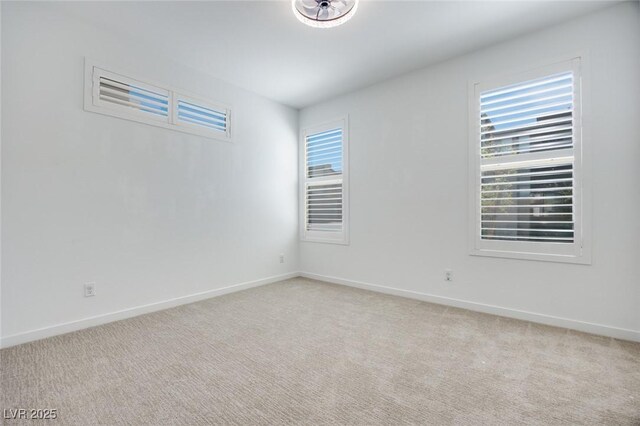spare room featuring light carpet, a wealth of natural light, and baseboards