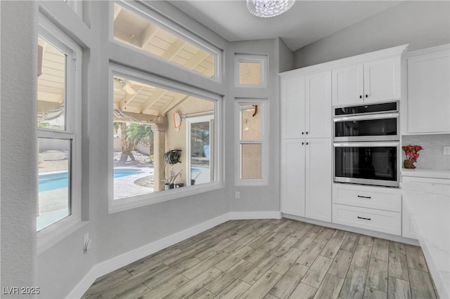 kitchen with stainless steel double oven, plenty of natural light, white cabinetry, and light wood-style flooring