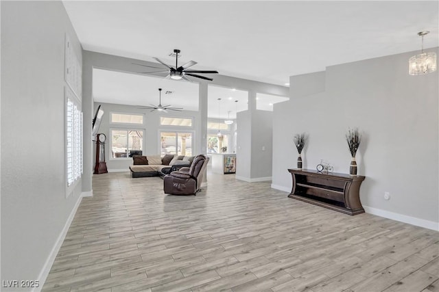 living room with light wood-type flooring, baseboards, and ceiling fan with notable chandelier