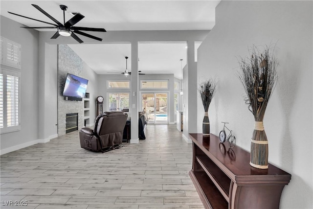 living area featuring baseboards, ceiling fan, lofted ceiling, a stone fireplace, and light wood-style flooring