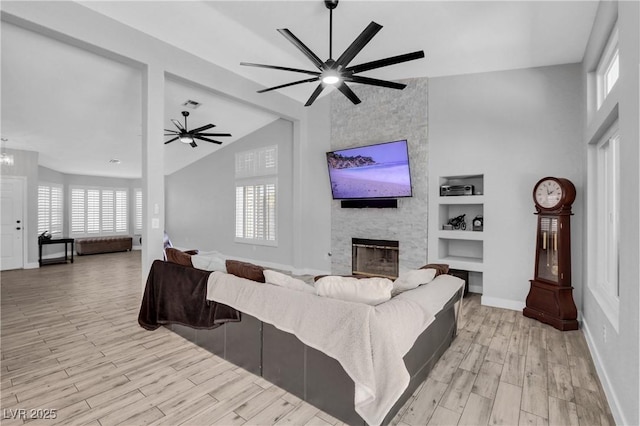 living room featuring a stone fireplace, built in features, light wood finished floors, and ceiling fan