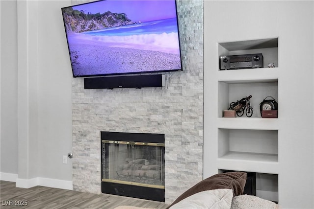 interior details featuring a stone fireplace, built in shelves, baseboards, and wood finished floors