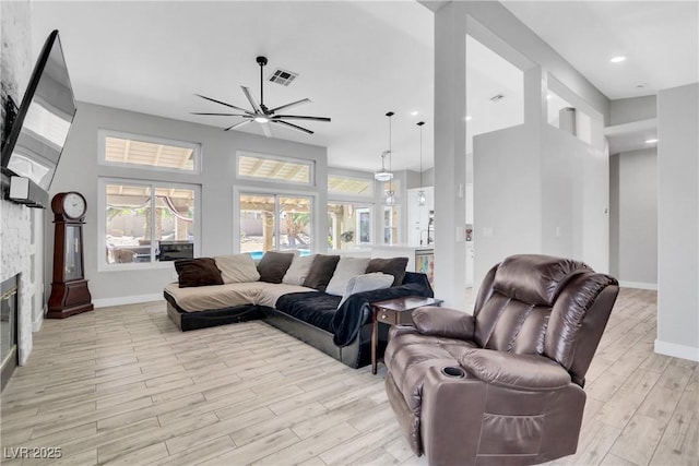 living room with a ceiling fan, baseboards, visible vents, a stone fireplace, and light wood-type flooring