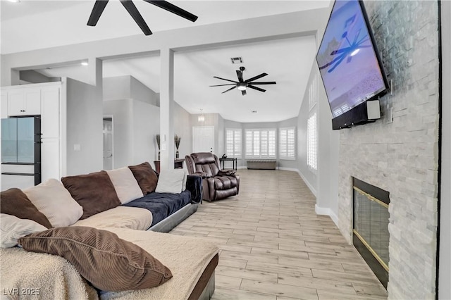 living area with lofted ceiling, a stone fireplace, light wood-style flooring, and a ceiling fan