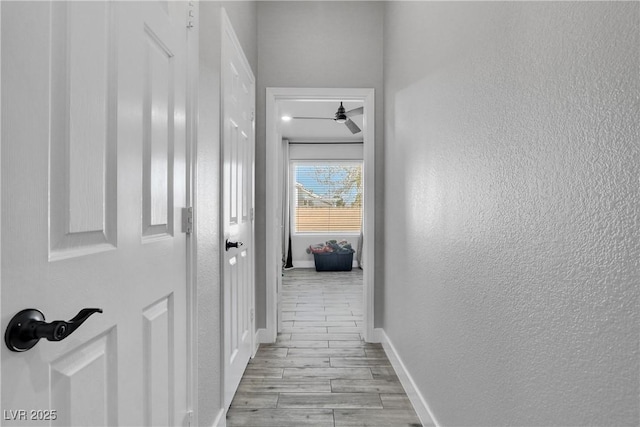 corridor featuring wood finish floors, baseboards, and a textured wall