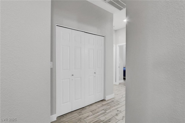 corridor featuring visible vents, baseboards, light wood-style floors, and a textured wall