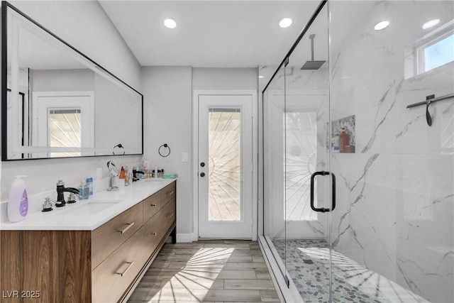 full bathroom with double vanity, wood finish floors, a marble finish shower, and a sink