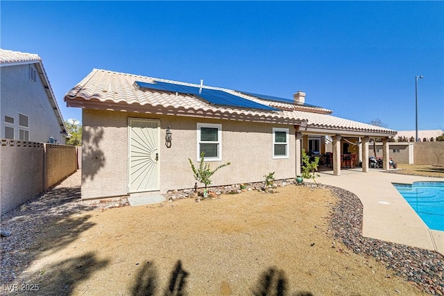 rear view of property with stucco siding, a tile roof, a fenced backyard, solar panels, and a patio area