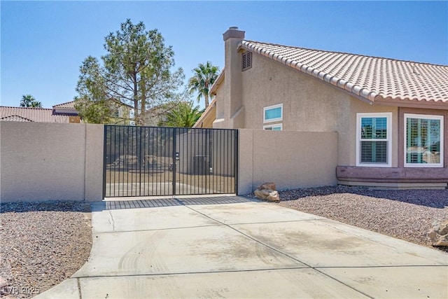 view of property exterior featuring a tiled roof, stucco siding, fence, and a gate