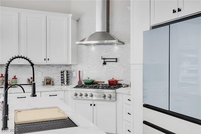 kitchen with stainless steel gas cooktop, white cabinets, wall chimney range hood, refrigerator with glass door, and backsplash