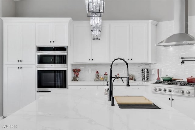 kitchen featuring tasteful backsplash, white cabinets, stainless steel appliances, and wall chimney range hood