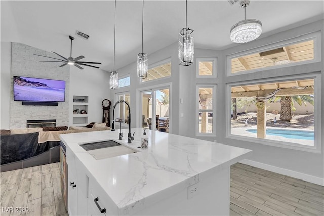 kitchen with light stone counters, visible vents, light wood-style flooring, ceiling fan, and a sink