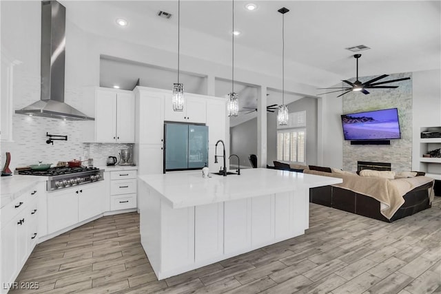 kitchen with a ceiling fan, a sink, wall chimney range hood, stainless steel gas stovetop, and light countertops