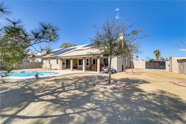 rear view of house featuring solar panels, a fenced in pool, fence, a patio area, and a gate