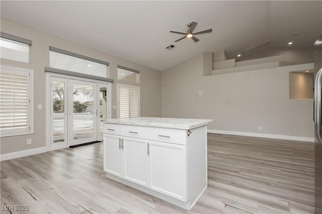 kitchen featuring a ceiling fan, visible vents, a kitchen island, vaulted ceiling, and white cabinets