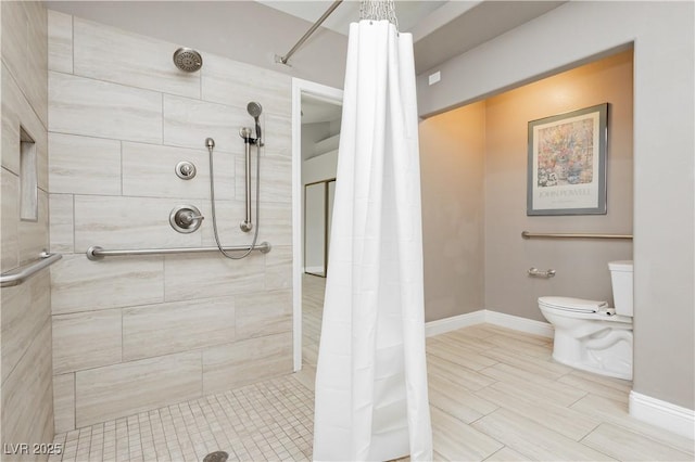 bathroom with toilet, tiled shower, and baseboards