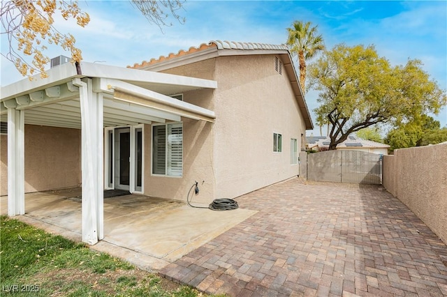 back of property featuring fence, a tile roof, stucco siding, a patio area, and a gate