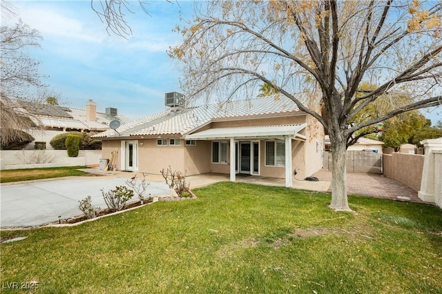 rear view of property featuring stucco siding, a patio, a lawn, and fence