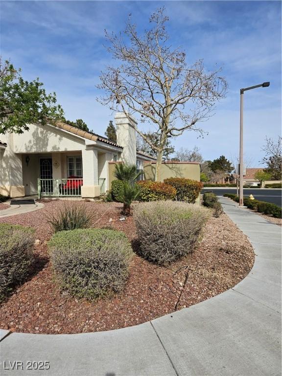 view of side of home with a tiled roof, stucco siding, a porch, and a chimney