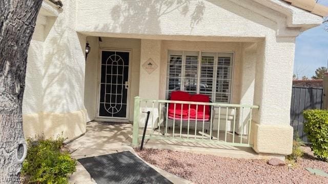 entrance to property featuring stucco siding and fence