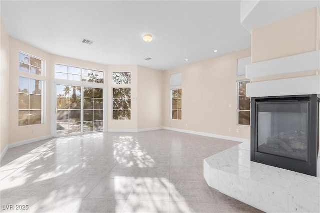 unfurnished living room featuring a multi sided fireplace, visible vents, a healthy amount of sunlight, and baseboards