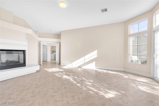 unfurnished living room featuring visible vents, a multi sided fireplace, baseboards, and washer / clothes dryer