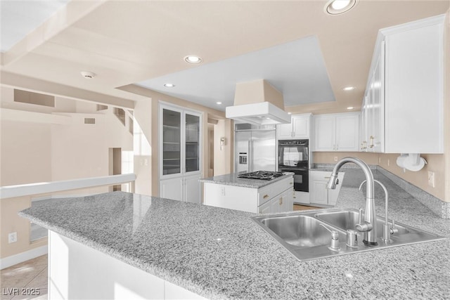 kitchen with recessed lighting, a sink, built in refrigerator, dobule oven black, and white cabinetry